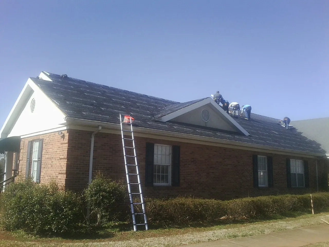 Crew tearing shingles off a brick ranch roof with a ladder set — Emergency Roof Repair work by our crew in Brownville
