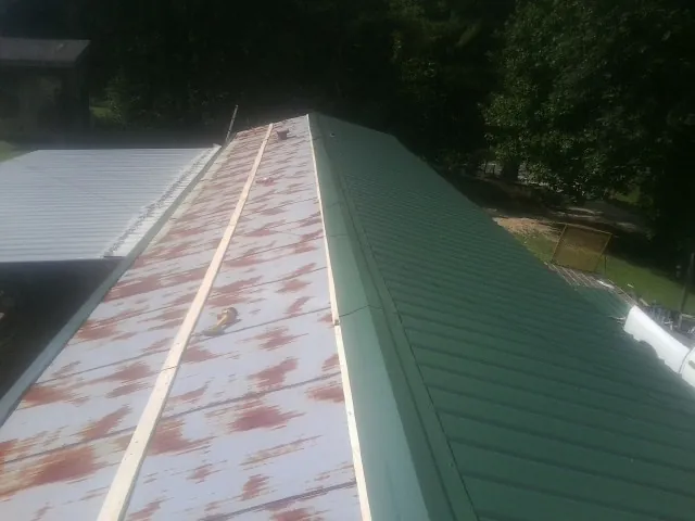 Old rusted panels beside newly installed green metal roofing — Wind Damage Roof Repair by Roofing Brothers in Brownville